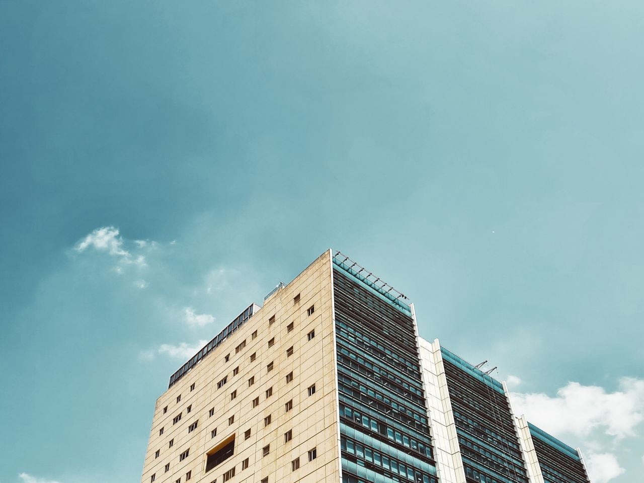 Low-angle view of a beige office building and a glass tower against a clear sky.
